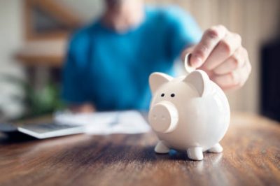 Man putting a coin into a pink piggy bank concept for savings and finance